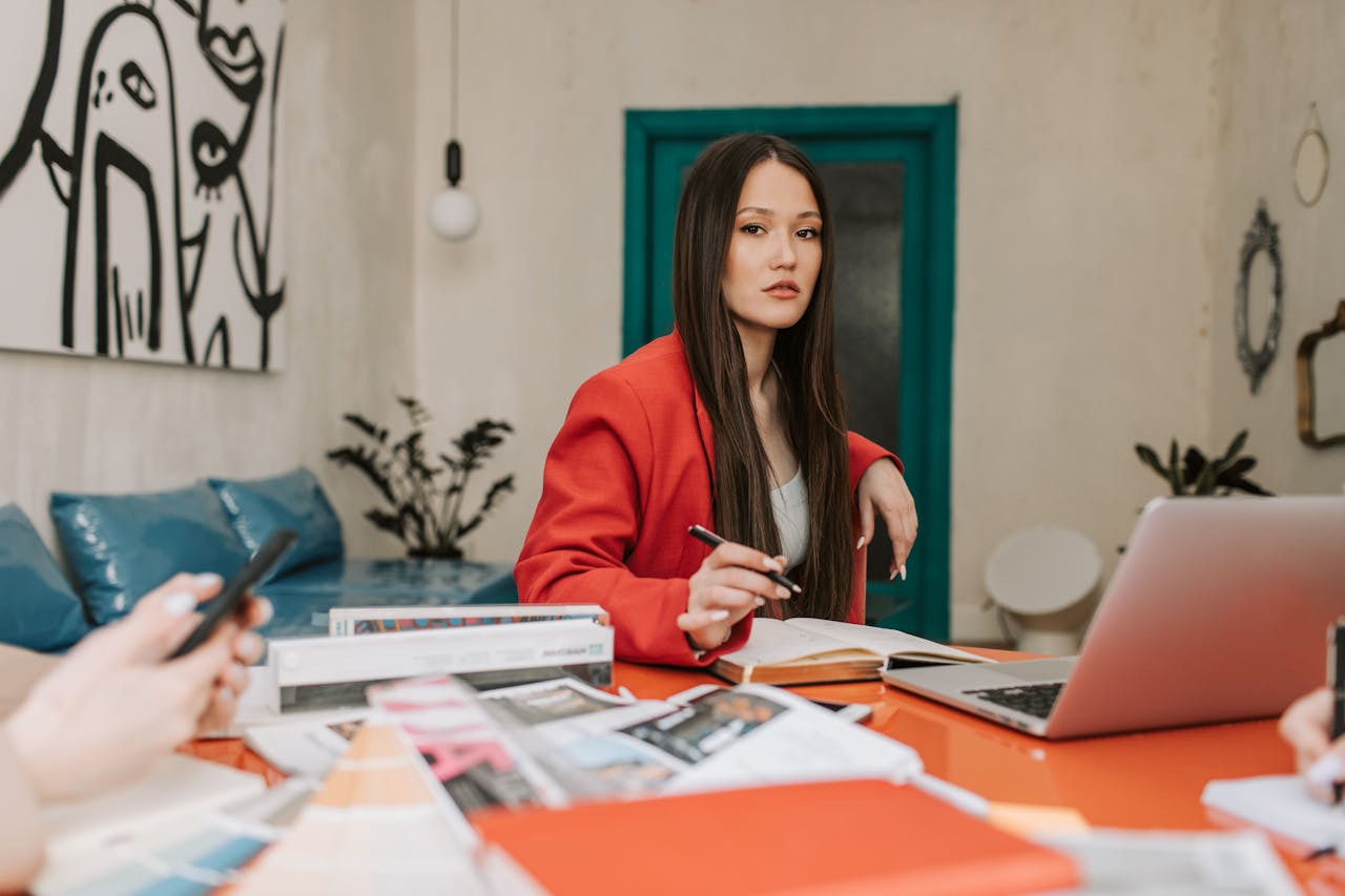 why-choose-us Professional woman in a red blazer working with colleagues in a modern office space.